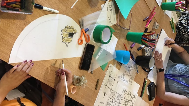 Image of a worktable with sketchbooks, coloured pens and materials.
